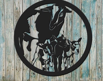 May include: Black metal silhouette of a goat and three kids in a circular frame. The goat is standing with its head turned to the side, and the kids are standing in front of it. The silhouette is cut out of a metal sheet and mounted on a wooden background.