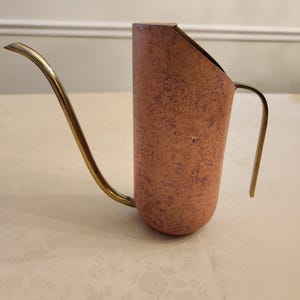 Puede incluir: Una regadera de estilo vintage con un cuerpo de color cobre y un pico largo y delgado de lat&oacute;n. La regadera tiene forma cil&iacute;ndrica con un asa lateral. El cuerpo tiene un acabado texturizado con motas moradas. El pico y el asa son de lat&oacute;n brillante.