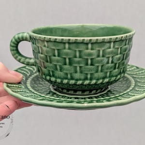 May include: Green ceramic teacup and saucer set. The cup has a basket weave design, and the saucer has a scalloped edge with a leaf pattern. The set is a vintage style and is a solid green color.