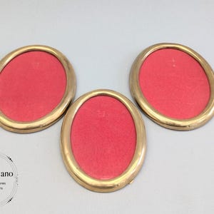 May include: Three gold-coloured oval picture frames with red felt backing.