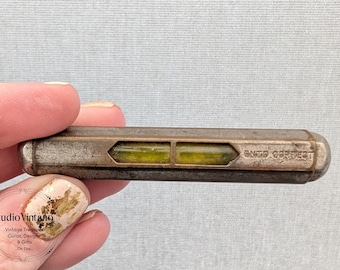 May include: A vintage level tool with a rectangular shape and two green liquid-filled vials. The metal casing has a tarnished appearance, with the text "GNTS CORRECT" visible on the side. The tool is held by a person.