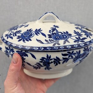 May include: A white porcelain serving dish with a blue and white floral pattern. The dish has a lid and two handles.