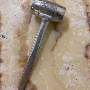 May include: A silver mallet with a cylindrical head and a long, slender handle. The head features an engraved design. The mallet is made of metal and is designed for use in various crafts or woodworking projects.