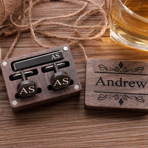 Puede incluir: Una caja de madera con un clip de corbata negro y gemelos. La caja est&aacute; grabada con las iniciales "AS" y el nombre "Andrew".