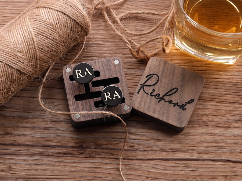 Puede incluir: Una caja de madera con tapa negra y dos gemelos negros con las iniciales "RA" grabadas. La caja tiene una peque&ntilde;a placa de madera en la parte delantera que dice "Richard".
