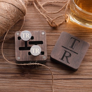 Puede incluir: Una caja de madera con dos gemelos de plata grabados con las iniciales "TR". La caja es de madera oscura y tiene una tapa con bisagras. Los gemelos est&aacute;n en la caja, y hay un peque&ntilde;o posavasos de madera con las iniciales "TR" grabadas en &eacute;l.