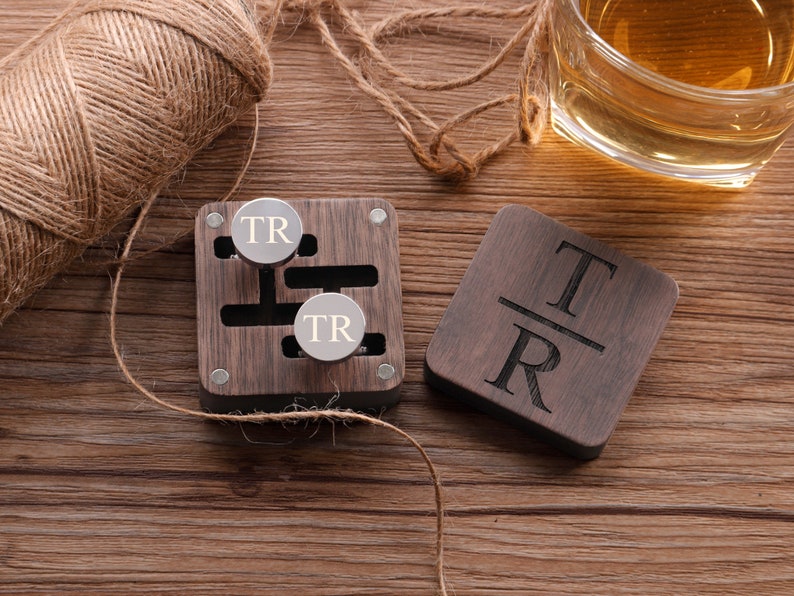 Puede incluir: Una caja de madera con dos gemelos de plata grabados con las iniciales "TR". La caja es de madera oscura y tiene una tapa con bisagras. Los gemelos est&aacute;n en la caja, y hay un peque&ntilde;o posavasos de madera con las iniciales "TR" grabadas en &eacute;l.