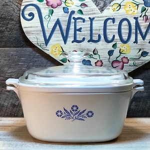May include: White ceramic casserole dish with a blue floral design and a glass lid. The dish has two handles on the sides.