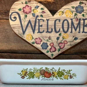 Puede incluir: Plato para hornear rectangular blanco con un diseño floral verde, amarillo y rojo. El plato tiene las palabras "L'echalote" impresas en la parte inferior.