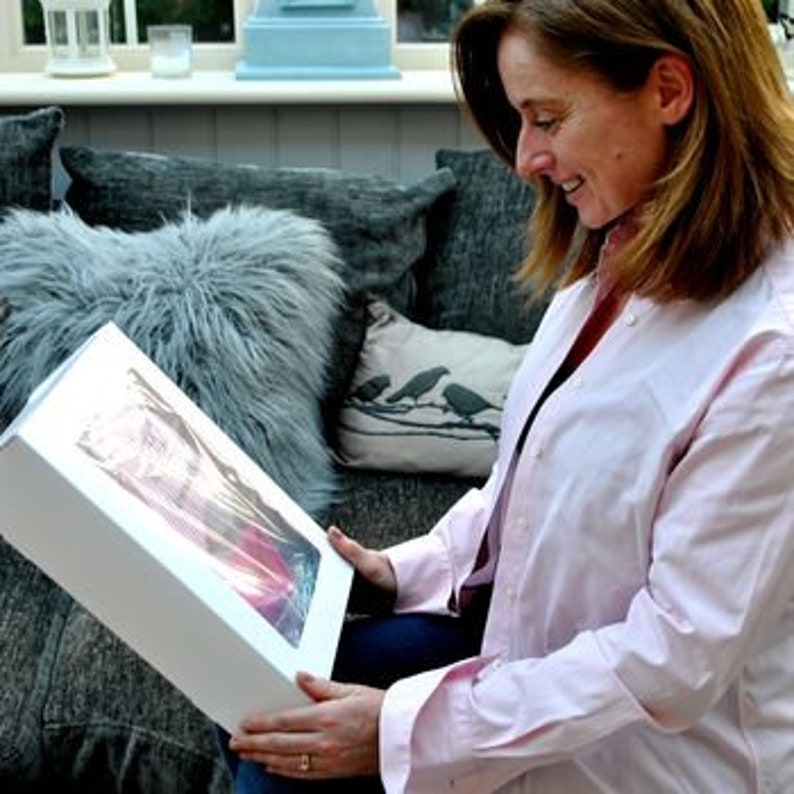 May include: A white box with a clear window showing a colorful abstract painting inside. The box is being held by a person.