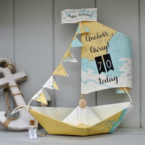 May include: A paper ship birthday decoration made from a nautical map with a banner that reads "Happy Birthday!" and "Anchors Away! 70 today".