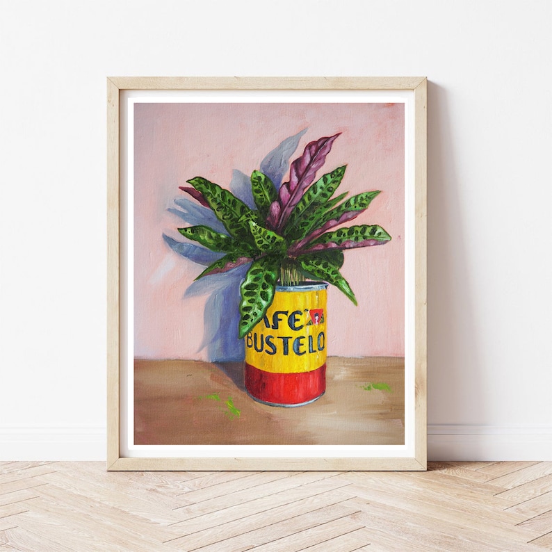 Puede incluir: Una pintura de una planta verde y morada en una lata amarilla y roja con el texto "Afeita Bustelo" en ella. La planta est&aacute; frente a una pared rosa.