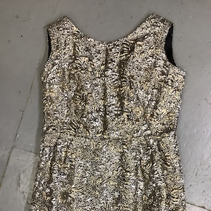 May include: A sleeveless gold and silver brocade dress with a round neckline. The dress has a fitted bodice and a slightly flared skirt.