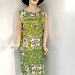 May include: A sleeveless, knee-length dress with a vibrant green and white geometric pattern. The dress features a scoop neckline and is paired with red flats and a brown hat. The dress is displayed on a mannequin.