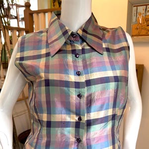 Puede incluir: Camisa sin mangas a cuadros en colores pastel. La camisa presenta un cuello clásico y una botonadura frontal. El estampado a cuadros incluye tonos de morado, azul, amarillo y verde. La camisa se exhibe en un maniquí.
