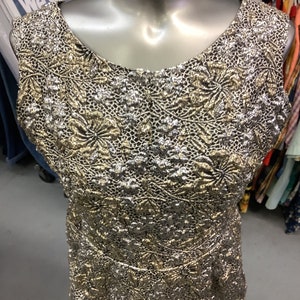 May include: A sleeveless gold and silver dress with a floral pattern. The dress is made of a textured fabric and has a fitted silhouette.