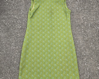 May include: A sleeveless, knee-length dress in a vibrant green hue, adorned with a delicate floral pattern in white and light blue. The dress features a round neckline and a subtle zipper detail. The overall design evokes a vintage aesthetic.