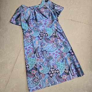 Puede incluir: Un vestido azul y morado con estampado paisley y mangas cortas. El vestido tiene un escote redondo y una silueta ajustada.