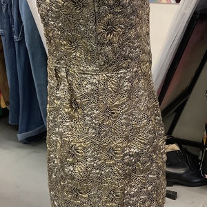 May include: A gold and silver sleeveless dress with a floral pattern. The dress is on a mannequin and is displayed in a store.