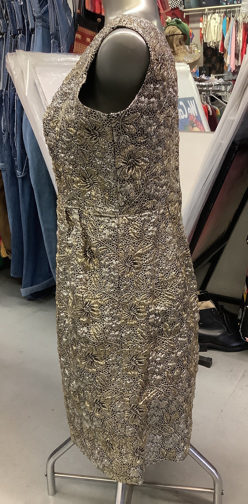 May include: A gold and silver sleeveless dress with a floral pattern. The dress is on a mannequin and is displayed in a store.