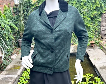 Puede incluir: Una blazer verde oscuro con cuello de terciopelo negro y tres botones negros. La blazer tiene un diseño sutil y dos bolsillos delanteros. El maniquí lleva un vestido negro debajo.