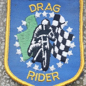 May include: A blue and gold embroidered patch featuring a motorcycle rider and the words "DRAG RIDER" surrounded by stars.