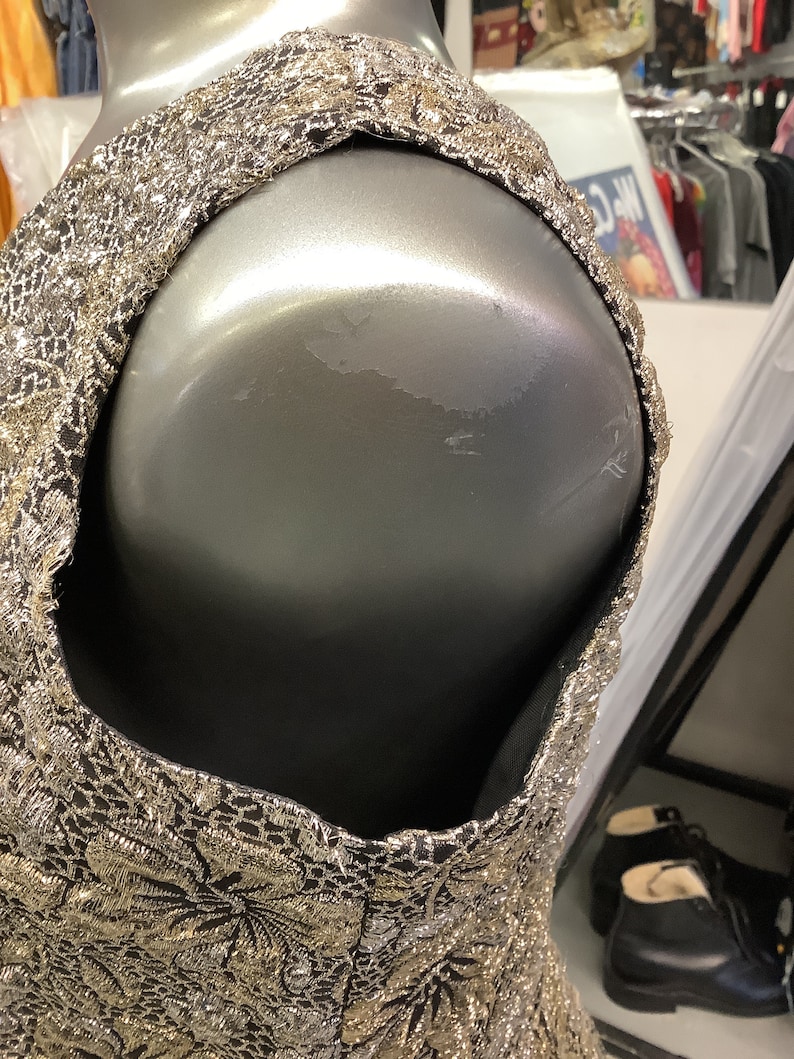May include: A sleeveless dress with a black and gold floral pattern. The dress is made of a shiny fabric and has a fitted bodice.