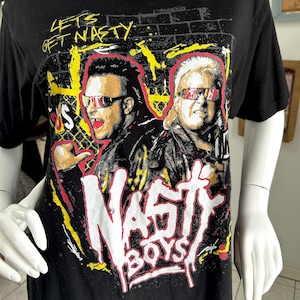 Könnte beinhalten: Schwarzes T-Shirt mit einer Grafik von zwei Männern mit Sonnenbrillen und den Worten "NASTY BOYS" in Weiß und Rot. Das Shirt hat auch den Text "LETS GET NASTY" in Gelb und Weiß.