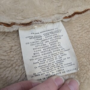 May include: Close-up of a tag from Valdor Sportswear Co. The tag lists the materials of the garment, including genuine leather, polyester, wool, and textile fibers. The tag also includes cleaning instructions and is marked "Made in Canada."