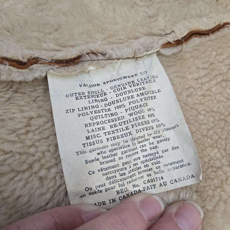 May include: Close-up of a tag from Valdor Sportswear Co. The tag lists the materials of the garment, including genuine leather, polyester, wool, and textile fibers. The tag also includes cleaning instructions and is marked "Made in Canada."