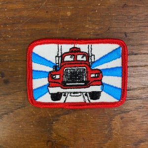 May include: Red and white embroidered patch of a red semi-truck with a blue and white striped background.