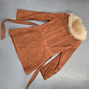 May include: A brown suede jacket with a faux fur collar and a tie belt. The jacket has a pleated design on the back and long sleeves. The jacket is approximately 30 inches long.