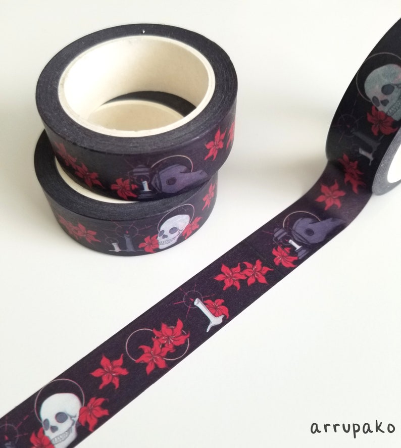 May include: Black washi tape with a repeating pattern of red flowers, skulls, and candles. The tape is rolled up and ready to be used.