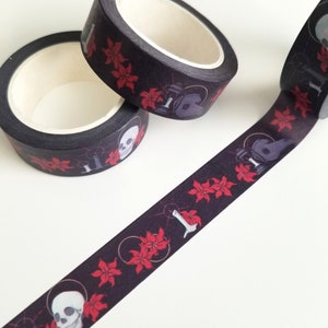 May include: Black washi tape with a repeating pattern of red flowers, skulls, and candles. The tape is rolled up and partially unrolled, showing the design.