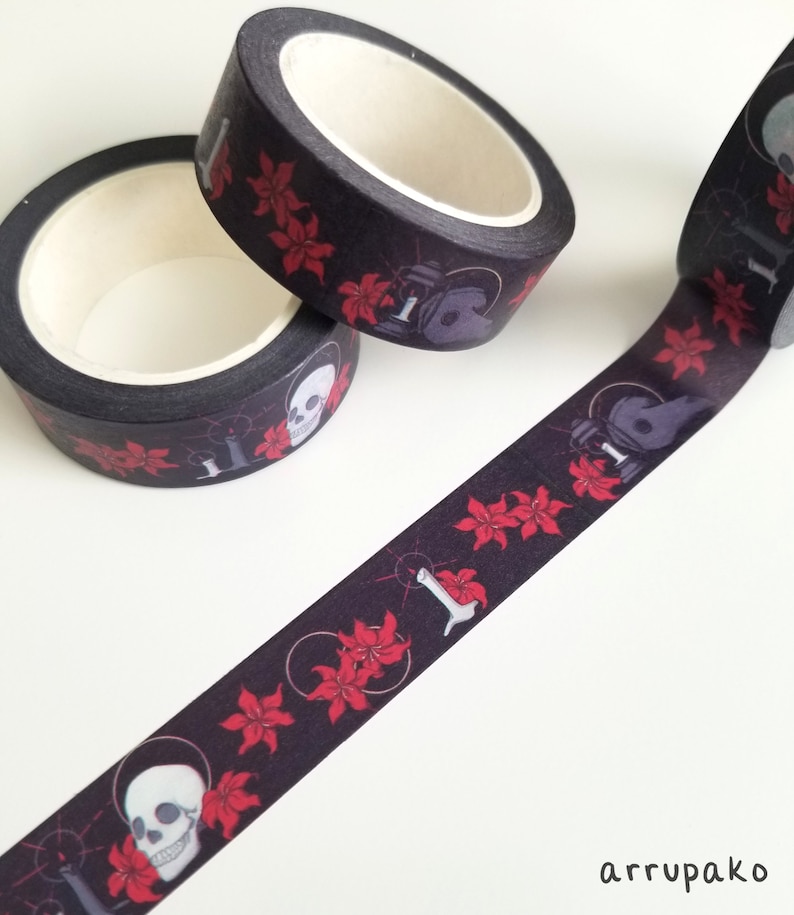 May include: Black washi tape with a repeating pattern of red flowers, skulls, and candles. The tape is rolled up and partially unrolled, showing the design.