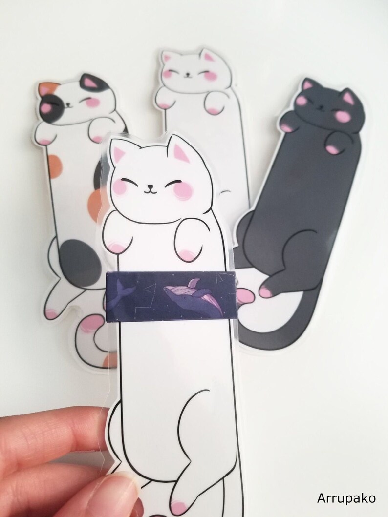 May include: Three cat-shaped bookmarks, one white, one black, and one calico. The white bookmark has a whale sticker on it.