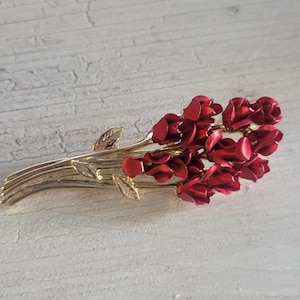 May include: A gold-toned brooch with a bouquet of red enamel roses. The roses are clustered together and have a slightly textured finish.