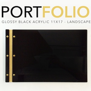 May include: Glossy black acrylic portfolio with a gold spine and brass accents. The portfolio is 11x17 inches and is landscape oriented. The text "PORTFOLIO" is printed in gold on the front of the portfolio.