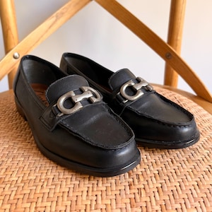 May include: A pair of black leather loafers featuring a silver-toned metal horsebit detail across the vamp. These slip-on shoes have a rounded toe, a low heel, and visible stitching along the apron, with the brand name Clarks visible inside.