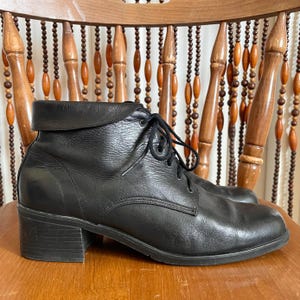 May include: Black leather ankle boots with a lace-up design and a small block heel. The boots have a rounded toe and a folded-over collar. The heel measures approximately 2 inches.