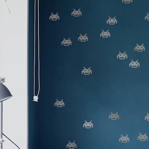 May include: A teal blue wall with a white bed in front of it. The wall is decorated with a pattern of gray space invaders.