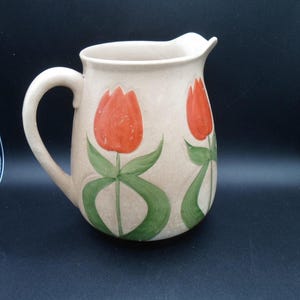 May include: A beige ceramic pitcher with a handle and a tulip design. The tulips are painted in shades of orange and green.