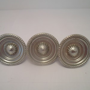 May include: Three silver-toned metal knobs with a raised, circular design and a beaded edge.
