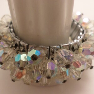 May include: A silver expandable bracelet with iridescent clear glass beads. The beads are faceted and have a sparkly finish.