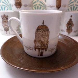 May include: A white porcelain teacup with a brown and gold illustration of a clock tower. The teacup is on a brown saucer.