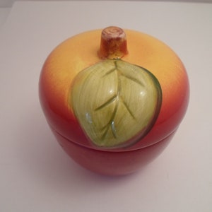 May include: A ceramic apple-shaped container with a lid. The apple is red with a yellow top and a green leaf painted on the side.