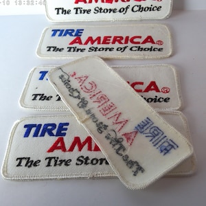 May include: Several white rectangular patches with embroidered text. The patches read "TIRE AMERICA" in red and blue, with "The Tire Store of Choice" below. One patch is partially obscured, showing the reverse side.