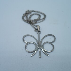 May include: A silver butterfly pendant necklace with a delicate chain. The pendant is a simple, open design with a thin, vertical bar in the center.