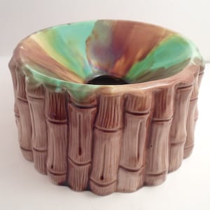 May include: A ceramic bowl with a bamboo-style exterior and a colorful interior. The exterior is a light brown color, with vertical lines mimicking bamboo stalks. The interior features shades of green, brown, and yellow.