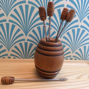 May include: A set of six wooden cocktail picks with metal prongs, stored in a wooden barrel-shaped holder. The holder is sitting on a wooden tray.